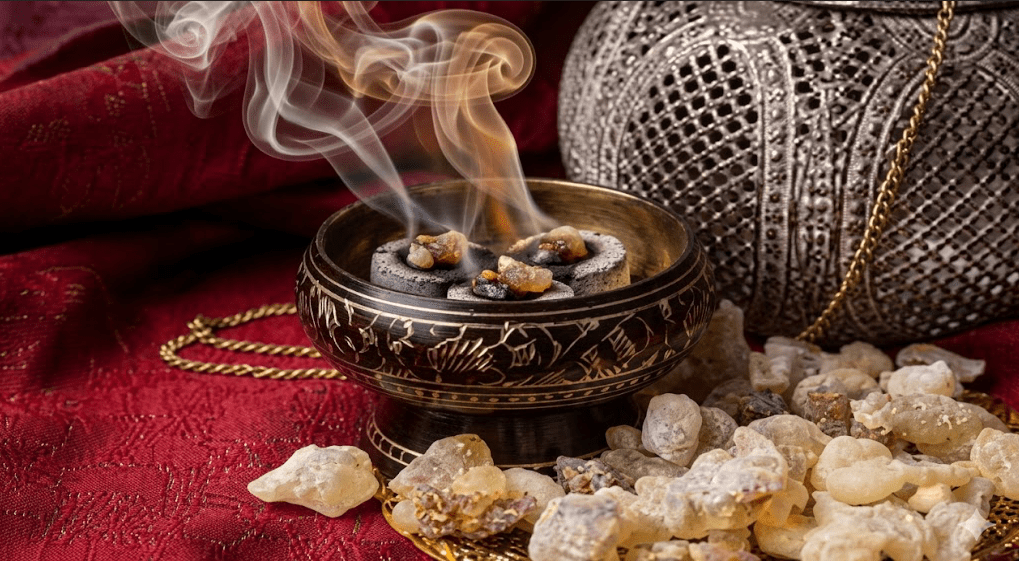 Overhead close-up of coarse white sea salt in a bowl and burning frankincense on a wooden kitchen counter, thin amber smoke rising