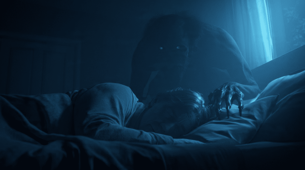 A person lying in bed asleep while a dark entity crouches at the head of the bed watching them, barely visible in the darkness