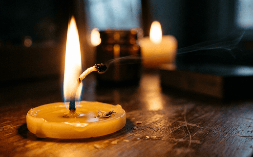 Close view of a candle flame with an overlong bent wick and a thin thread of smoke rising from the tip